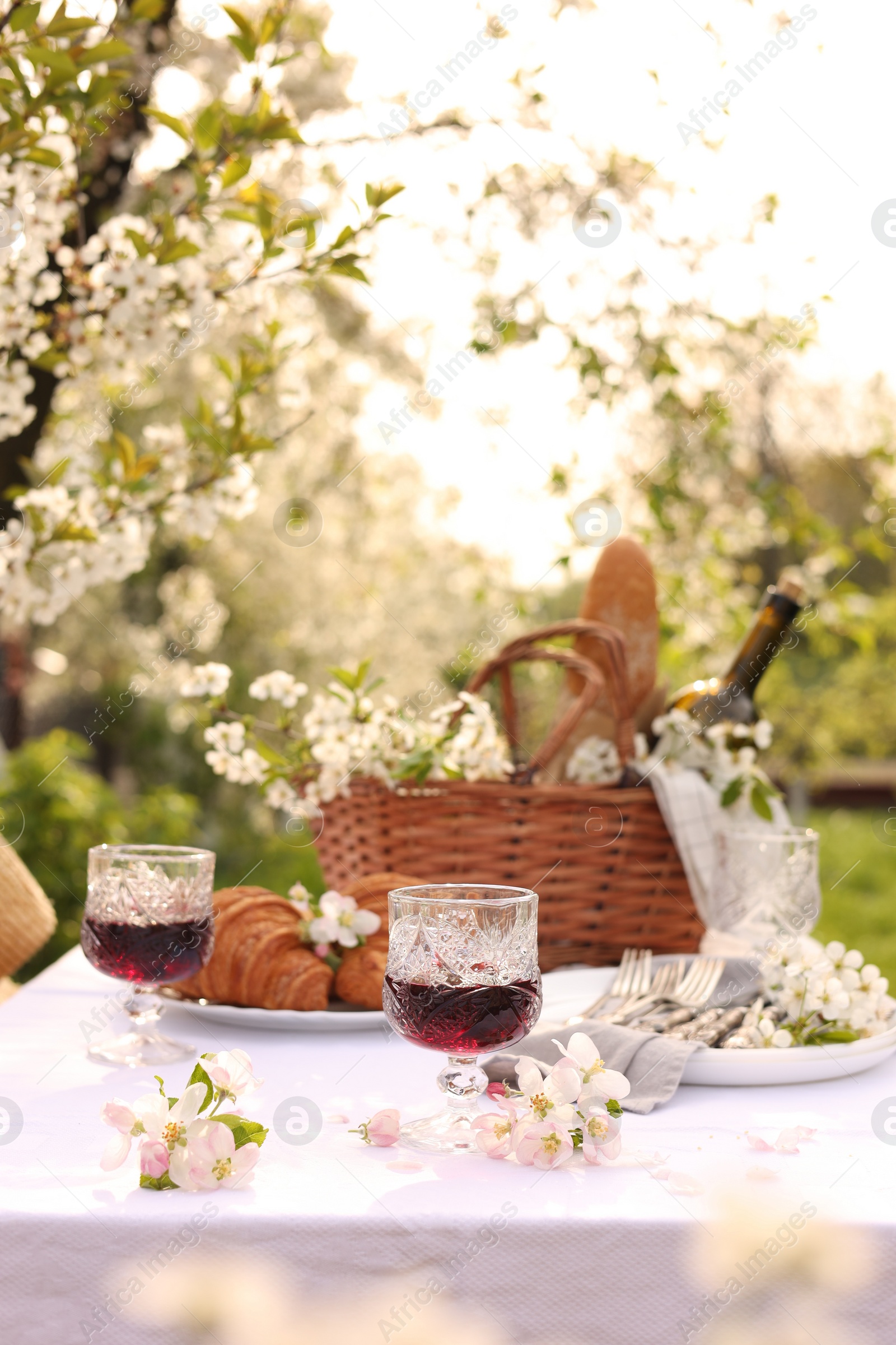 Photo of Stylish table setting with beautiful spring flowers, wine and croissants in garden