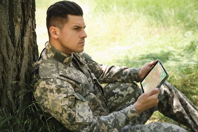 Photo of Soldier using tablet near tree in forest