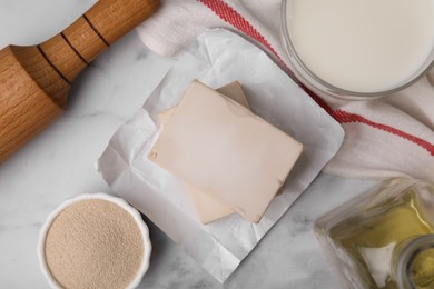 Yeast and ingredients for dough on white marble table, flat lay