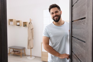 Happy man standing near door, space for text. Invitation to come indoors