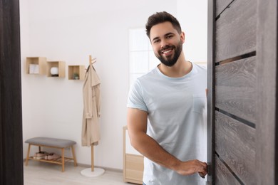 Photo of Happy man standing near door, space for text. Invitation to come indoors