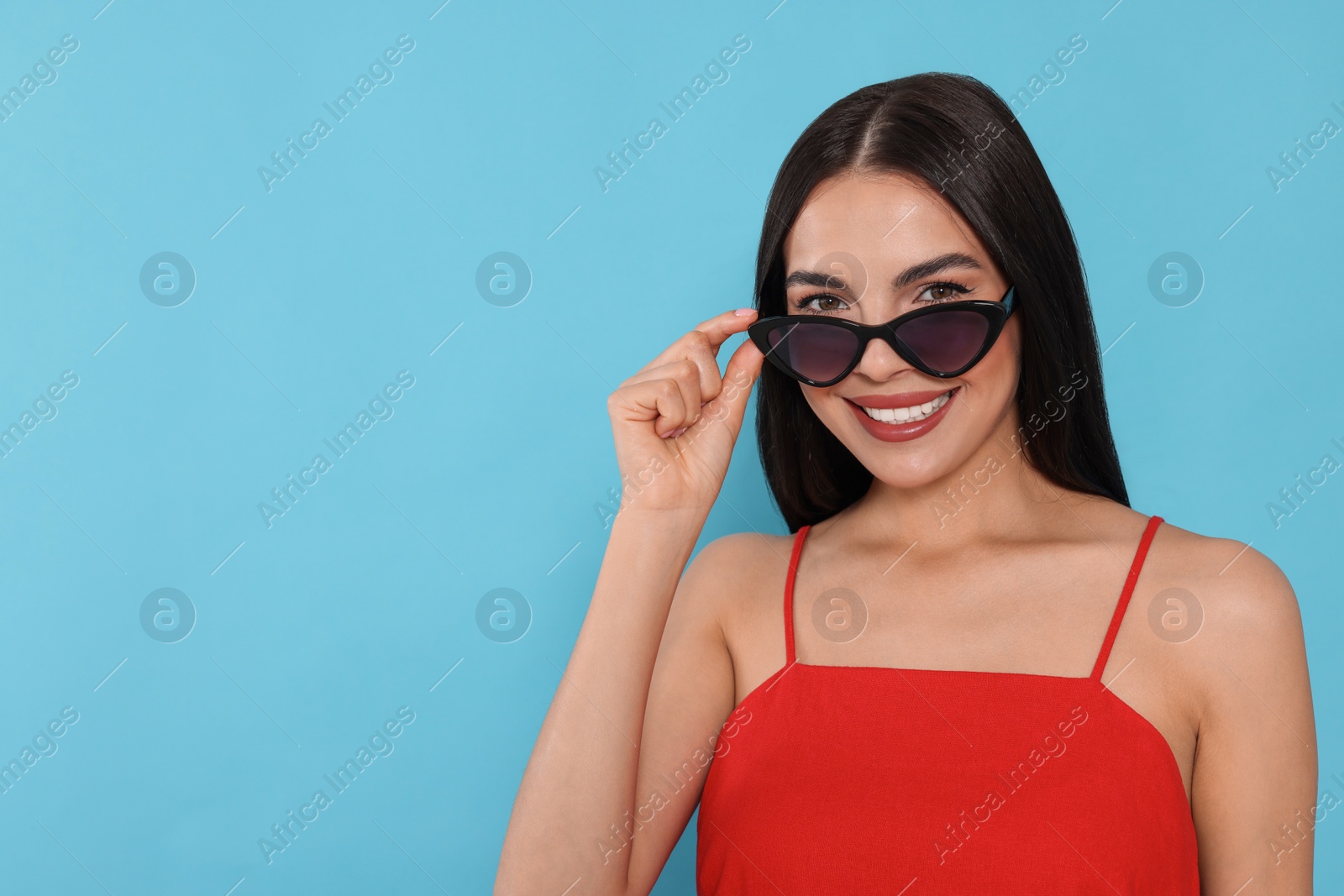 Photo of Attractive happy woman touching fashionable sunglasses against light blue background. Space for text