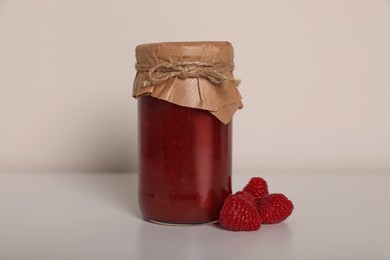 Photo of Tasty canned raspberry jam and fresh berries on white background