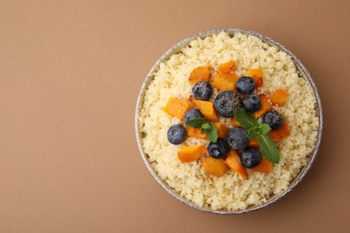 Photo of Bowl of tasty couscous with blueberries, pumpkin and mint on brown background, top view. Space for text
