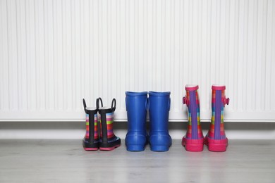 Photo of Different pairs of boots near modern radiator indoors