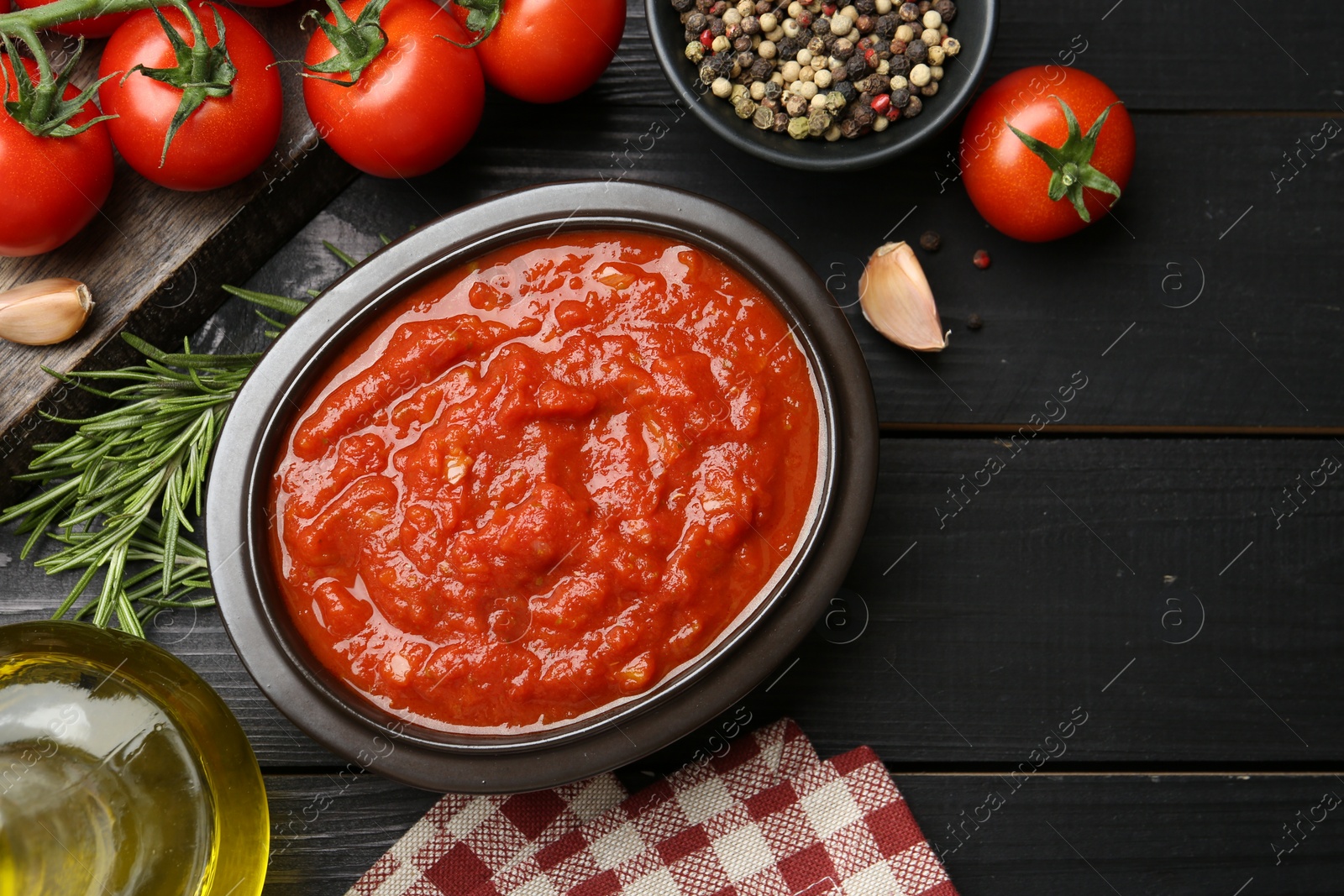 Photo of Homemade tomato sauce in bowl and fresh ingredients on black wooden table, flat lay