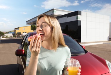 Photo of Beautiful young woman with juice eating doughnut near car at gas station