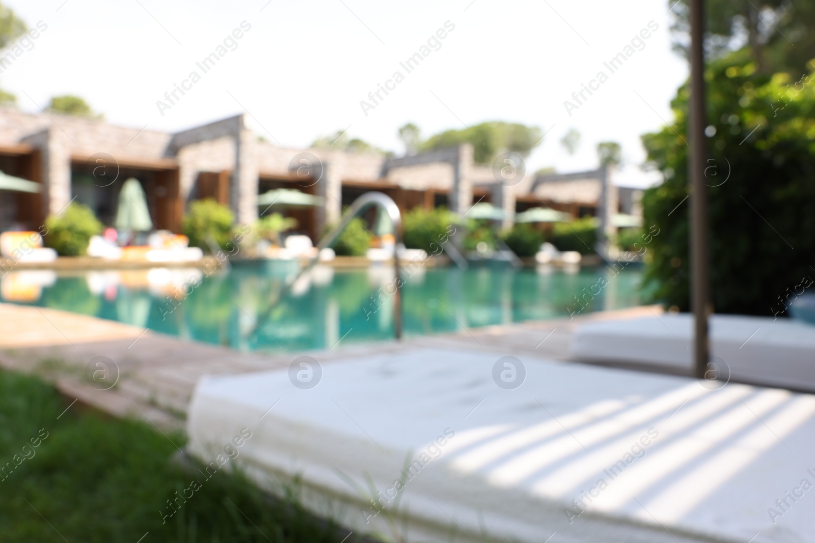 Photo of Sun loungers near outdoor swimming pool, blurred view. Luxury resort