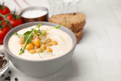 Tasty chickpea soup in bowl on white tiled table, closeup. Space for text