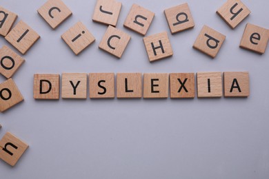 Wooden tiles with word Dyslexia on light grey background, flat lay. Space for text