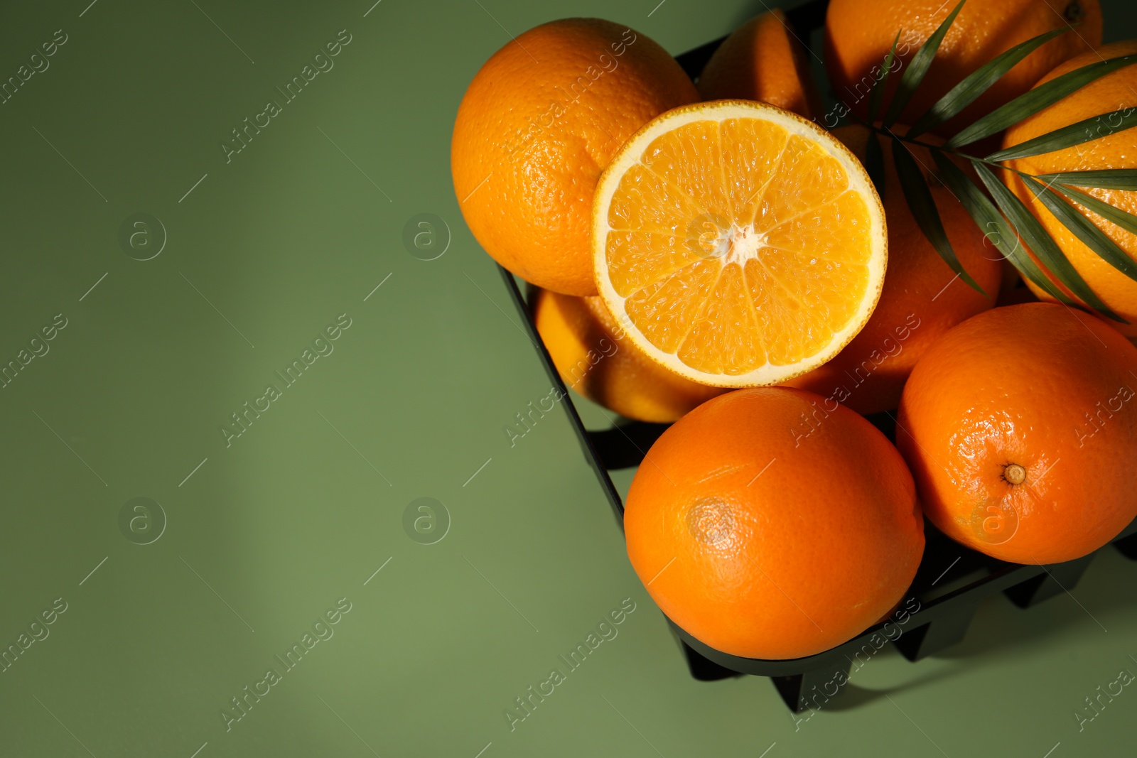 Photo of Fresh oranges in metal basket on green background, top view. Space for text