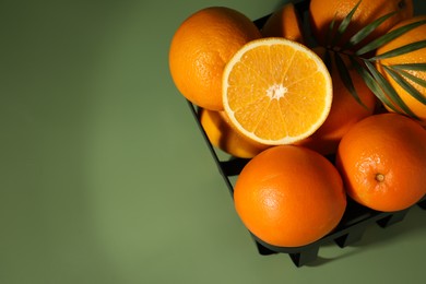 Fresh oranges in metal basket on green background, top view. Space for text