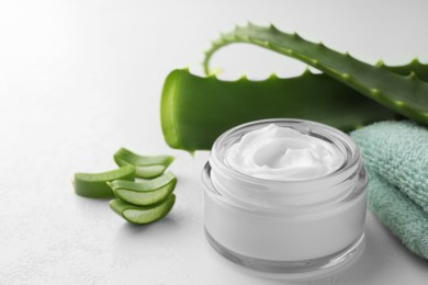 Photo of Jar with cream and cut aloe leaves on white table, closeup. Space for text