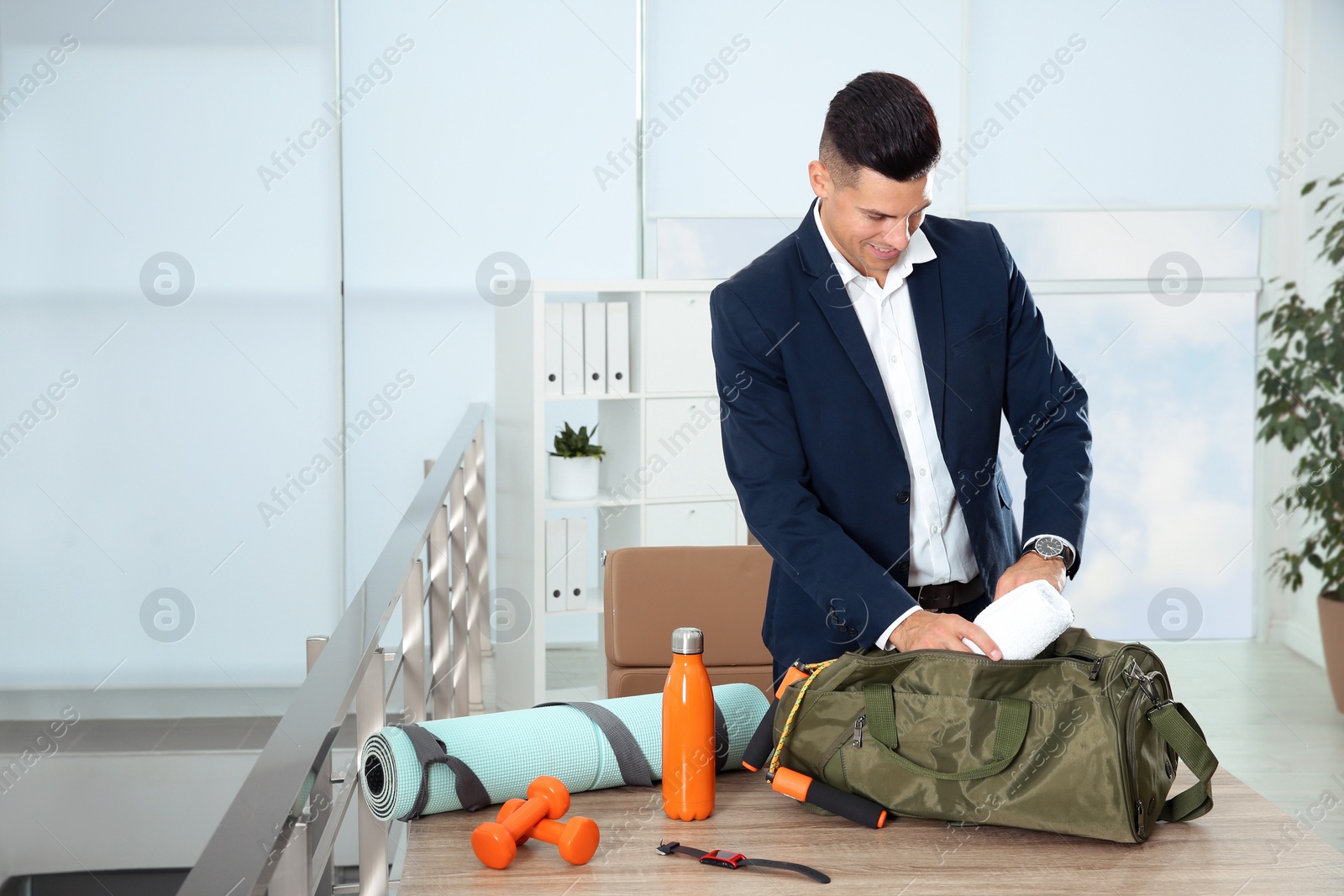 Photo of Businessman packing sports stuff for training into bag in office