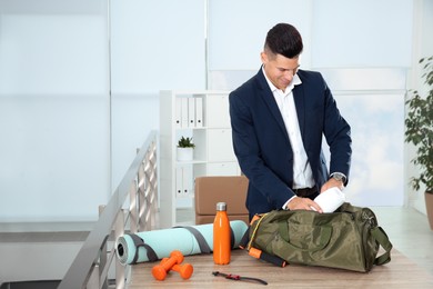 Businessman packing sports stuff for training into bag in office