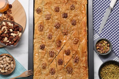 Photo of Delicious baklava with walnuts in baking pan and nuts on white table, flat lay