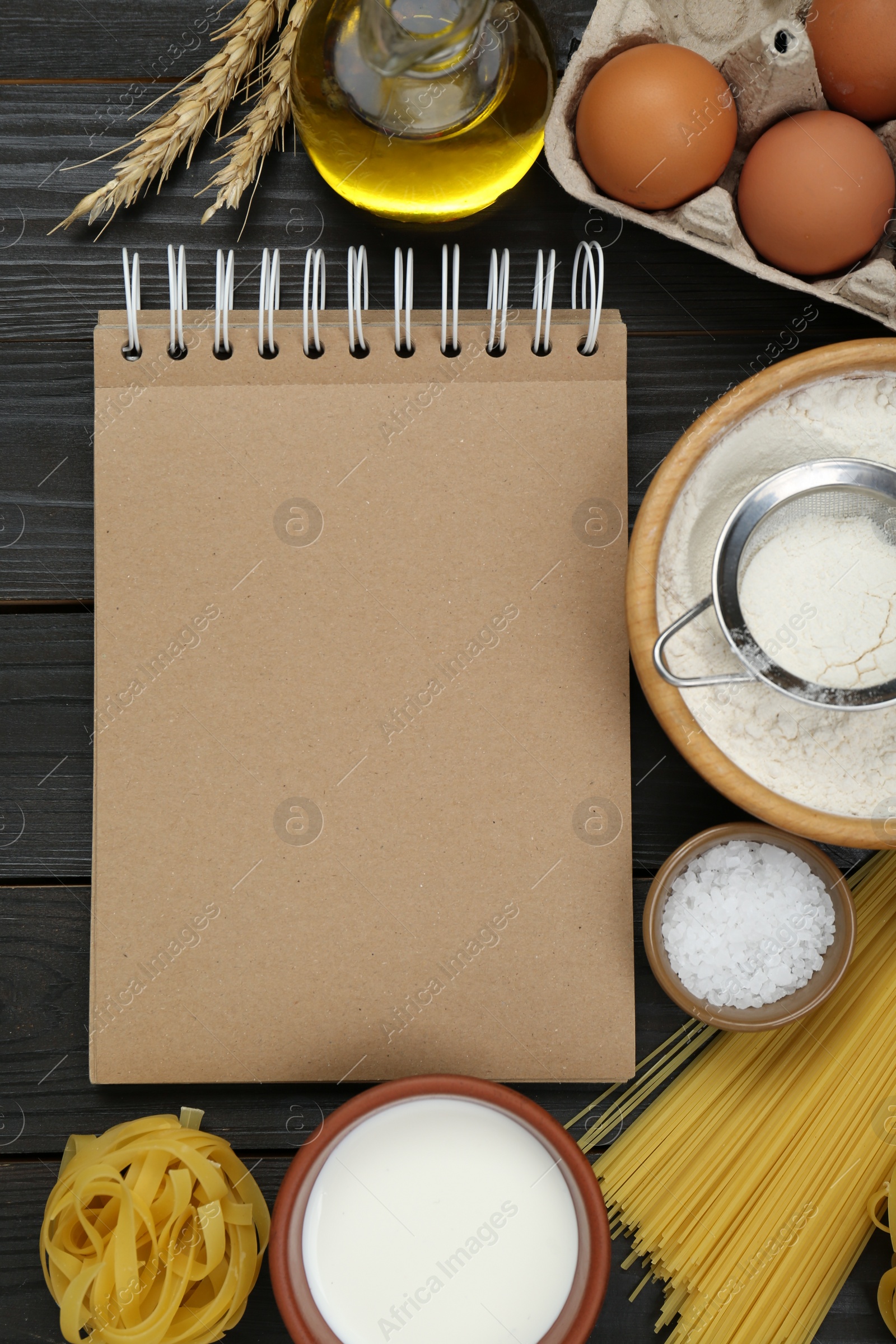 Photo of Blank recipe book and different ingredients on black wooden table, flat lay. Space for text