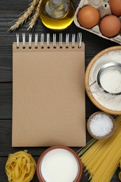 Blank recipe book and different ingredients on black wooden table, flat lay. Space for text