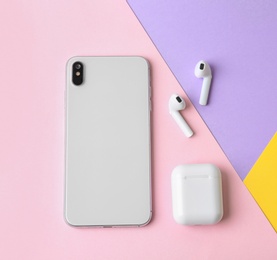 Photo of Wireless earphones, mobile phone and charging case on color background, flat lay