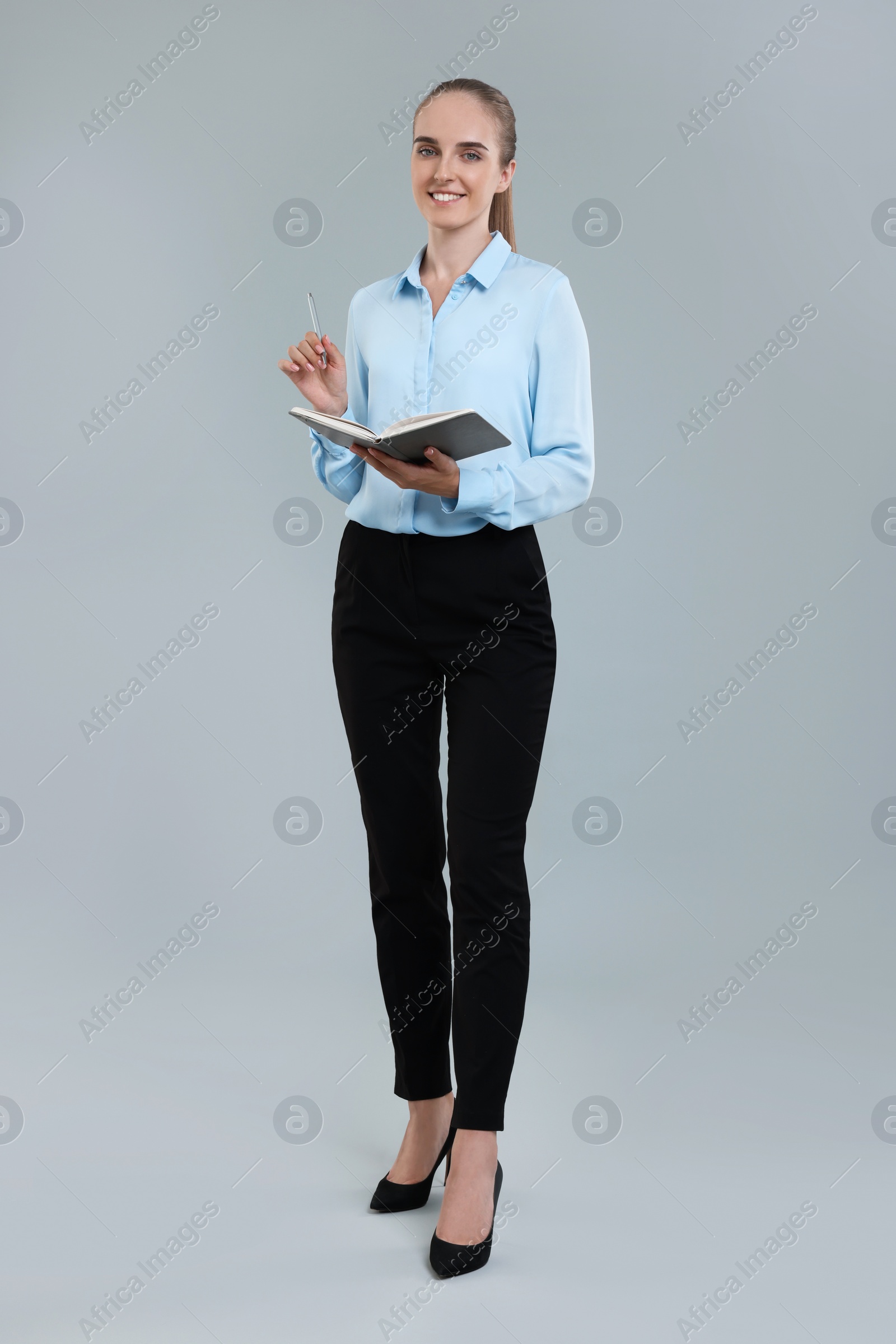 Photo of Happy young secretary with notebook and pen on grey background