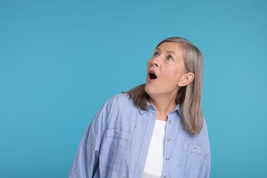 Portrait of surprised senior woman on light blue background, space for text
