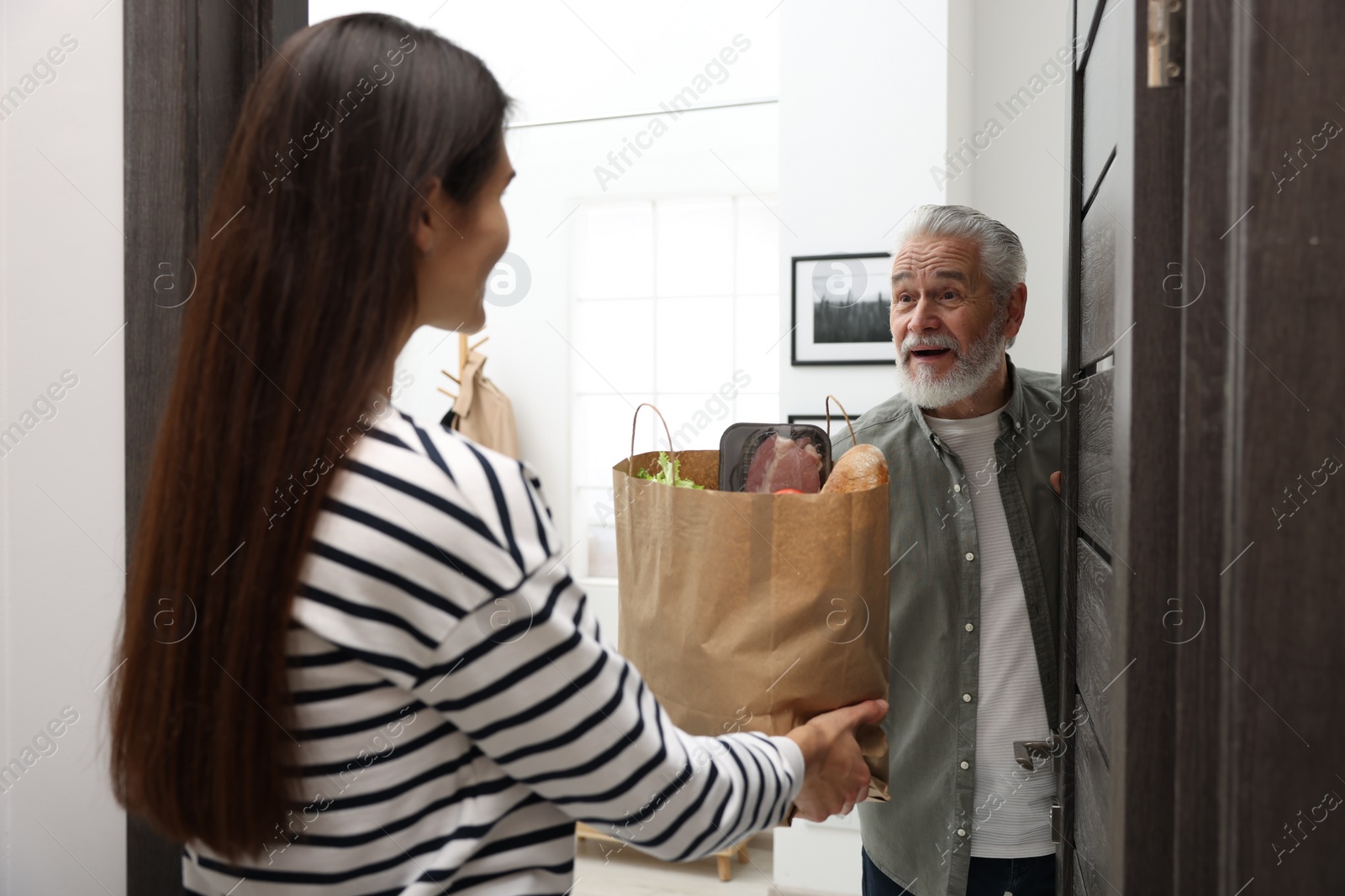 Photo of Courier giving paper bag with food products to senior man indoors