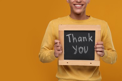Man holding small chalkboard with phrase Thank You on orange background, closeup. Space for text