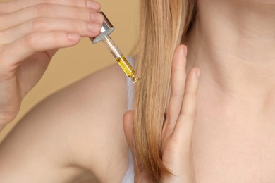 Photo of Woman applying essential oil onto hair on beige background, closeup