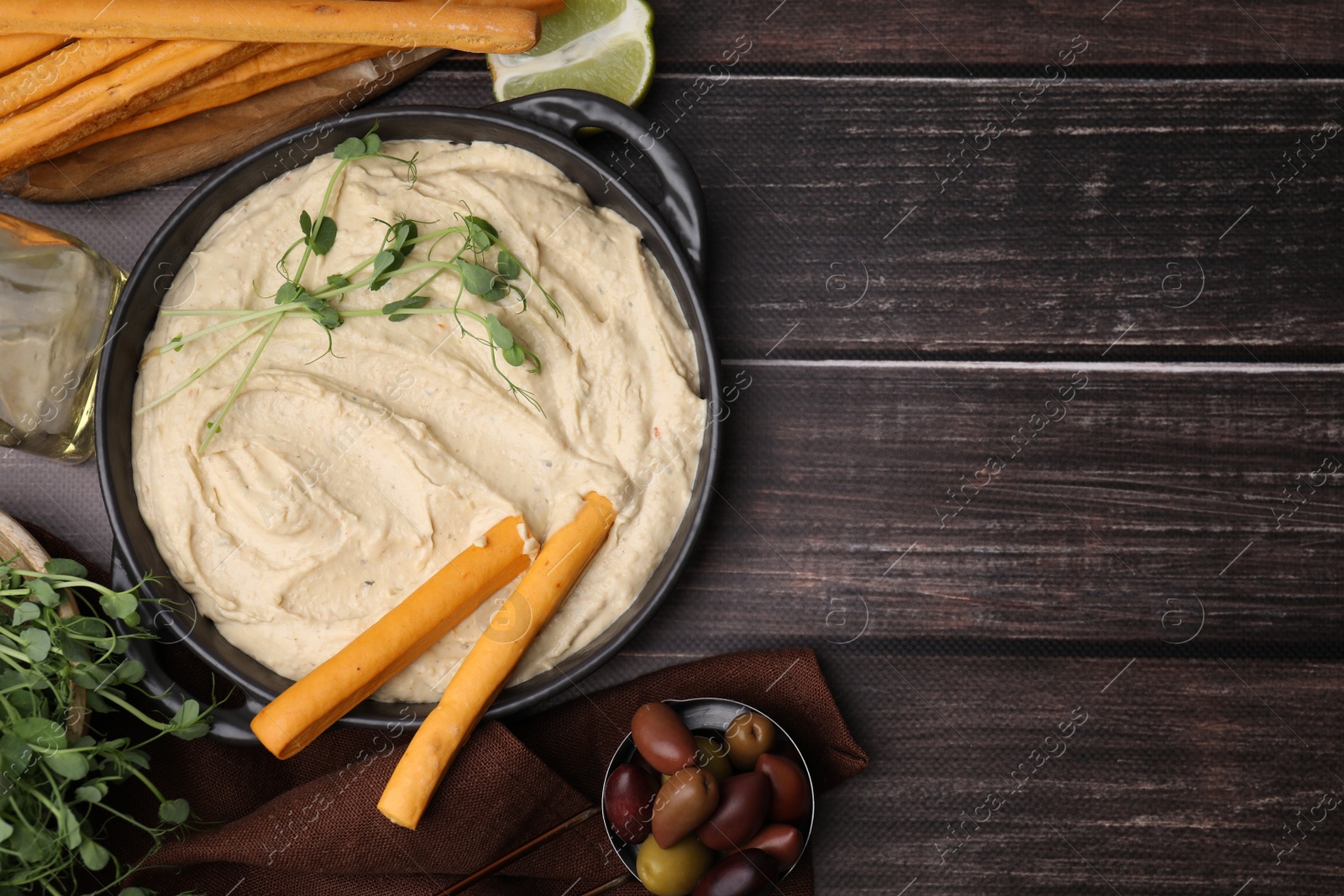 Photo of Delicious hummus with grissini sticks and ingredients on wooden table, flat lay. Space for text