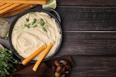Delicious hummus with grissini sticks and ingredients on wooden table, flat lay. Space for text