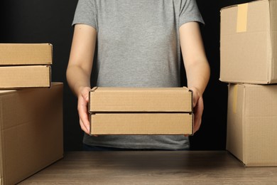 Photo of Packaging goods. Woman with cardboard boxes at wooden table, closeup