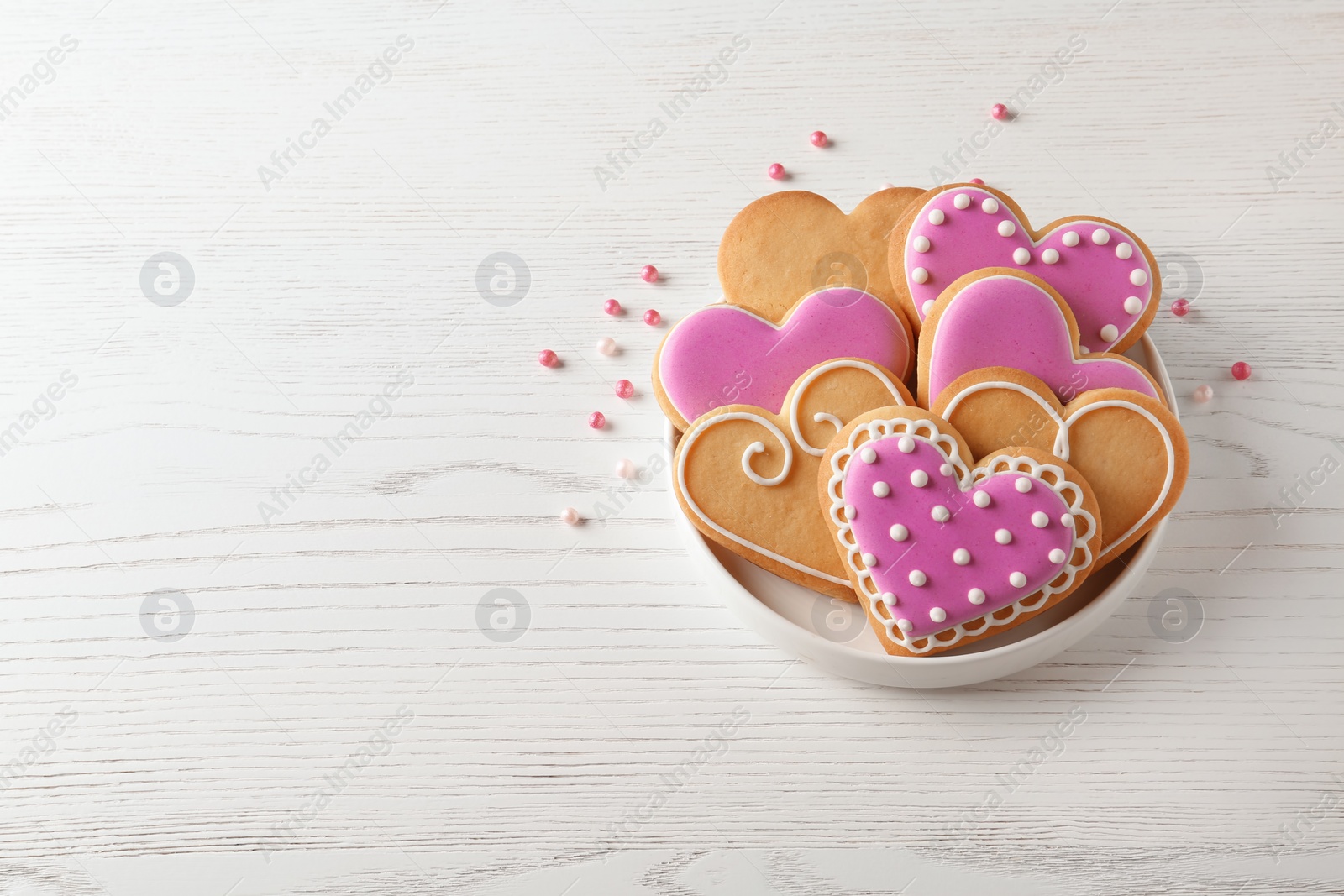 Photo of Plate with decorated heart shaped cookies on wooden table. Space for text