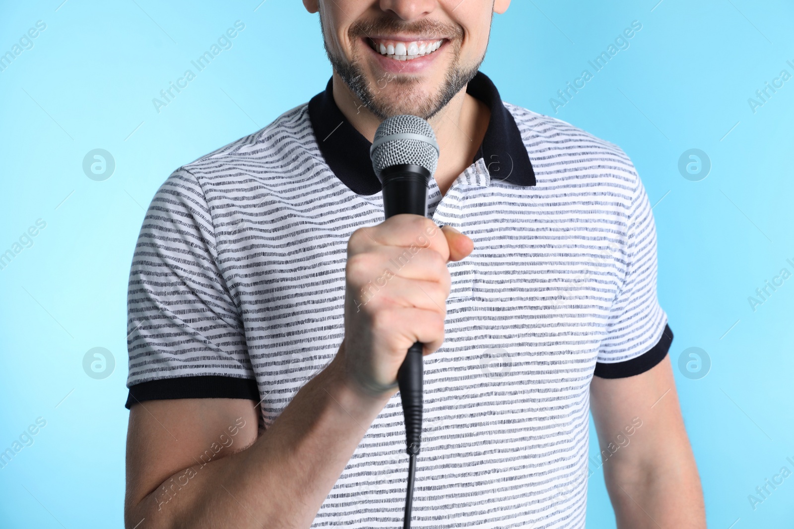 Photo of Handsome man in casual clothes holding microphone on color background, closeup