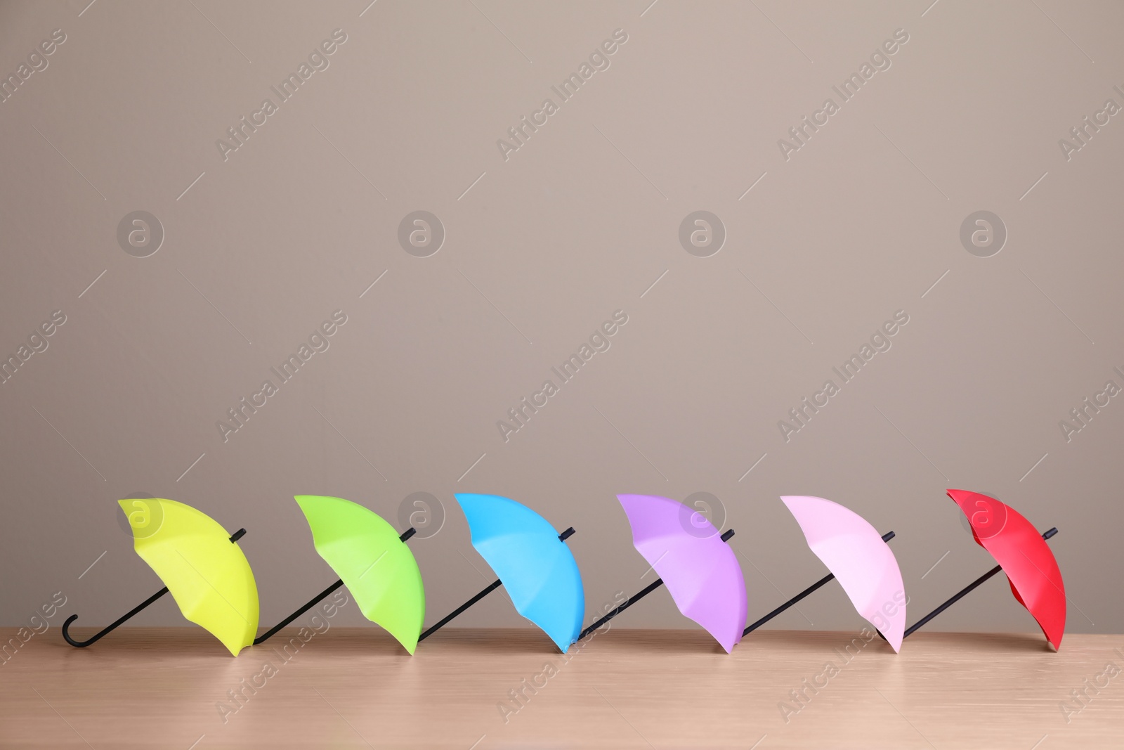 Photo of Small color umbrellas on wooden table against beige background. Space for text