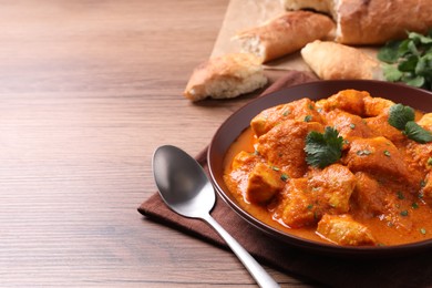 Photo of Bowl of delicious chicken curry on wooden table, space for text