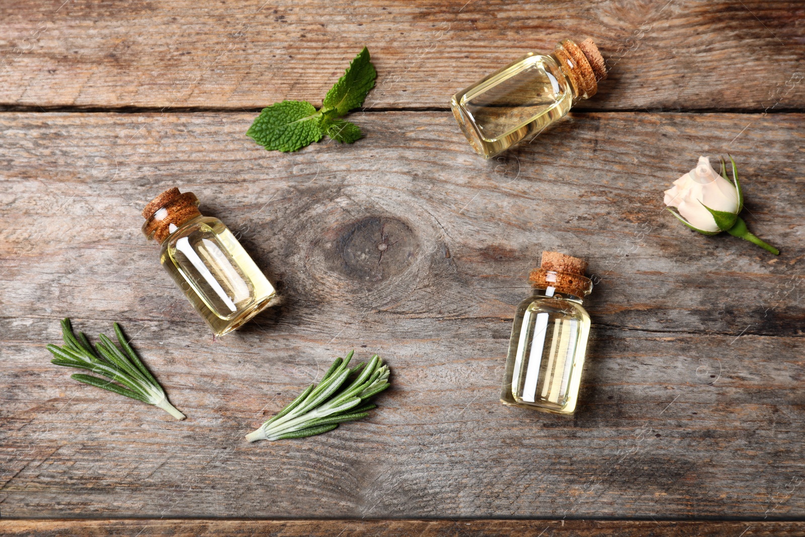 Photo of Different essential oils in glass bottles and ingredients on wooden background, flat lay