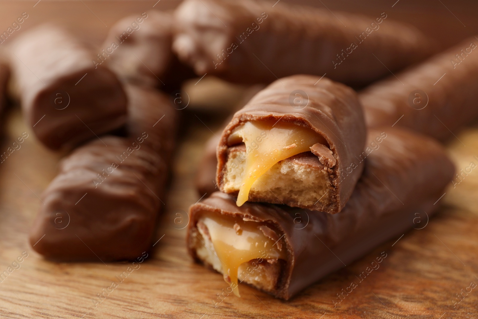Photo of Sweet tasty chocolate bars with caramel on wooden board, closeup. Space for text