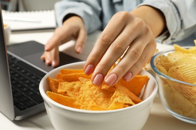 Photo of Bad habits. Woman eating tortilla chips while using laptop at table, closeup
