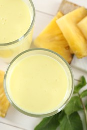 Photo of Tasty pineapple smoothie in glasses, mint and cut fruit on white table, flat lay