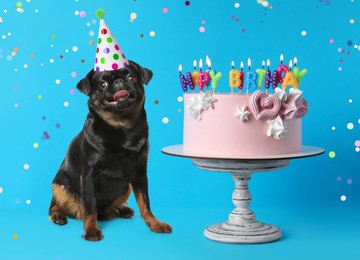 Image of Cute dog with party hat and delicious birthday cake on blue background