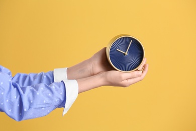 Young woman holding alarm clock on color background. Time concept