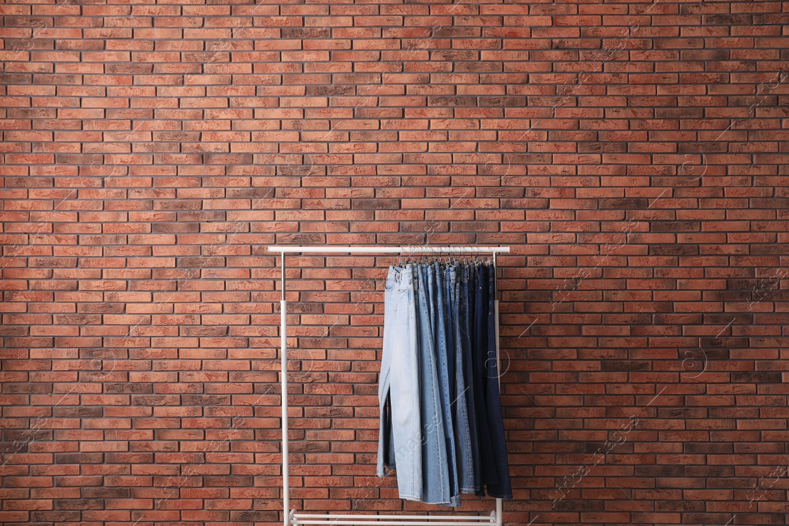 Photo of Rack with stylish jeans near brick wall