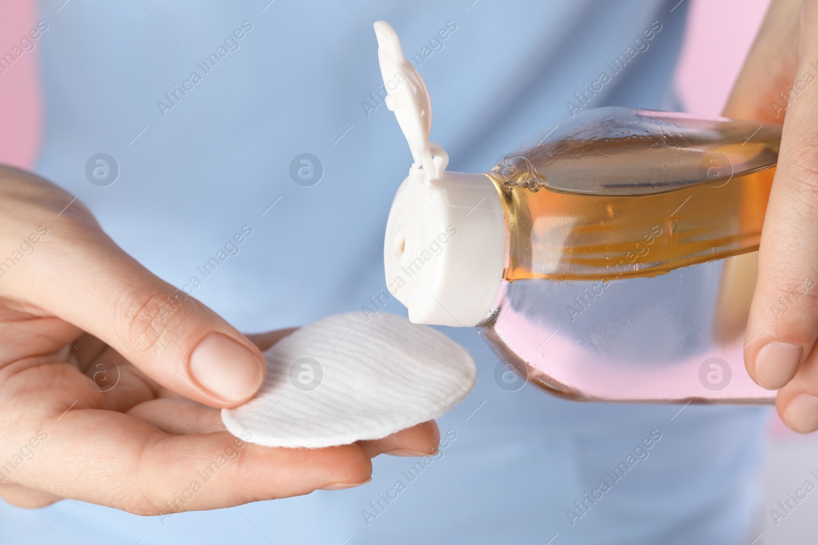 Photo of Woman pouring micellar water from bottle on cotton pad, closeup