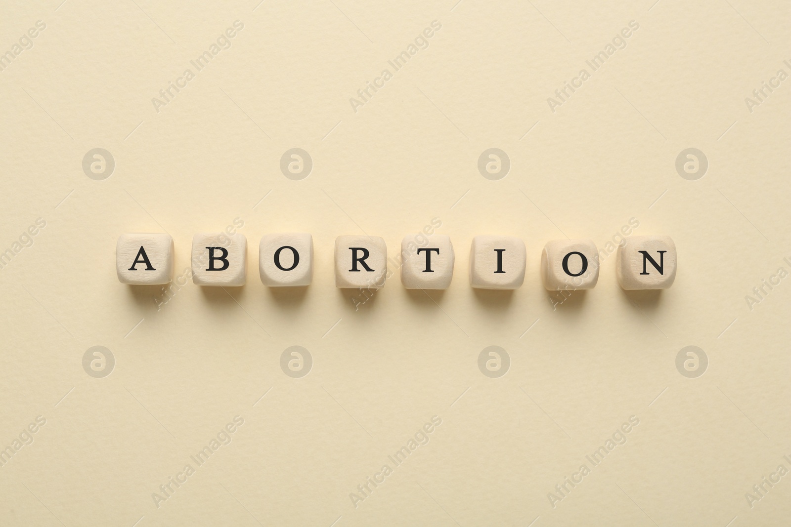 Photo of Word Abortion made of wooden cubes on beige background, flat lay