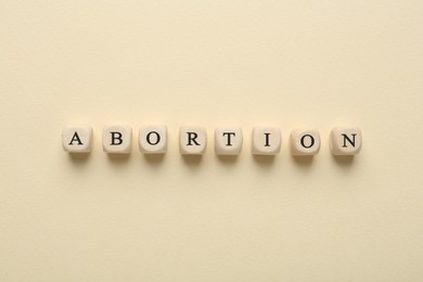 Photo of Word Abortion made of wooden cubes on beige background, flat lay