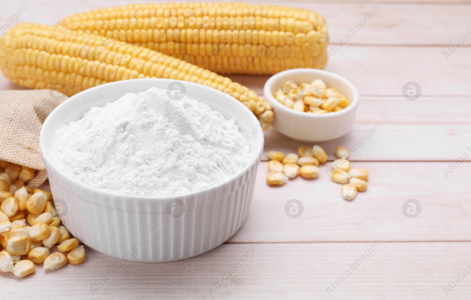 Photo of Bowl with corn starch, ripe cobs and kernels on wooden table. Space for text