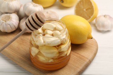 Photo of Honey with garlic in glass jar, lemons and dipper on white wooden table