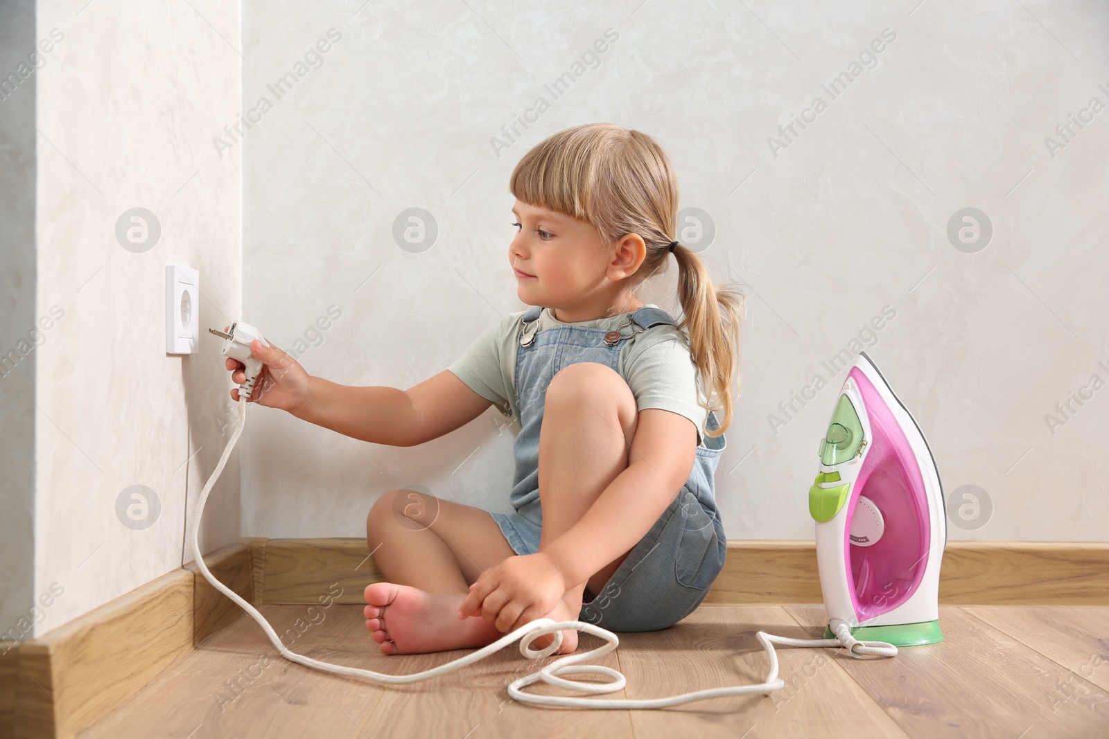 Photo of Little child playing with electrical socket and iron plug at home. Dangerous situation