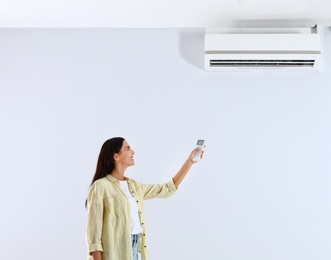 Photo of Young woman turning on air conditioner against white background