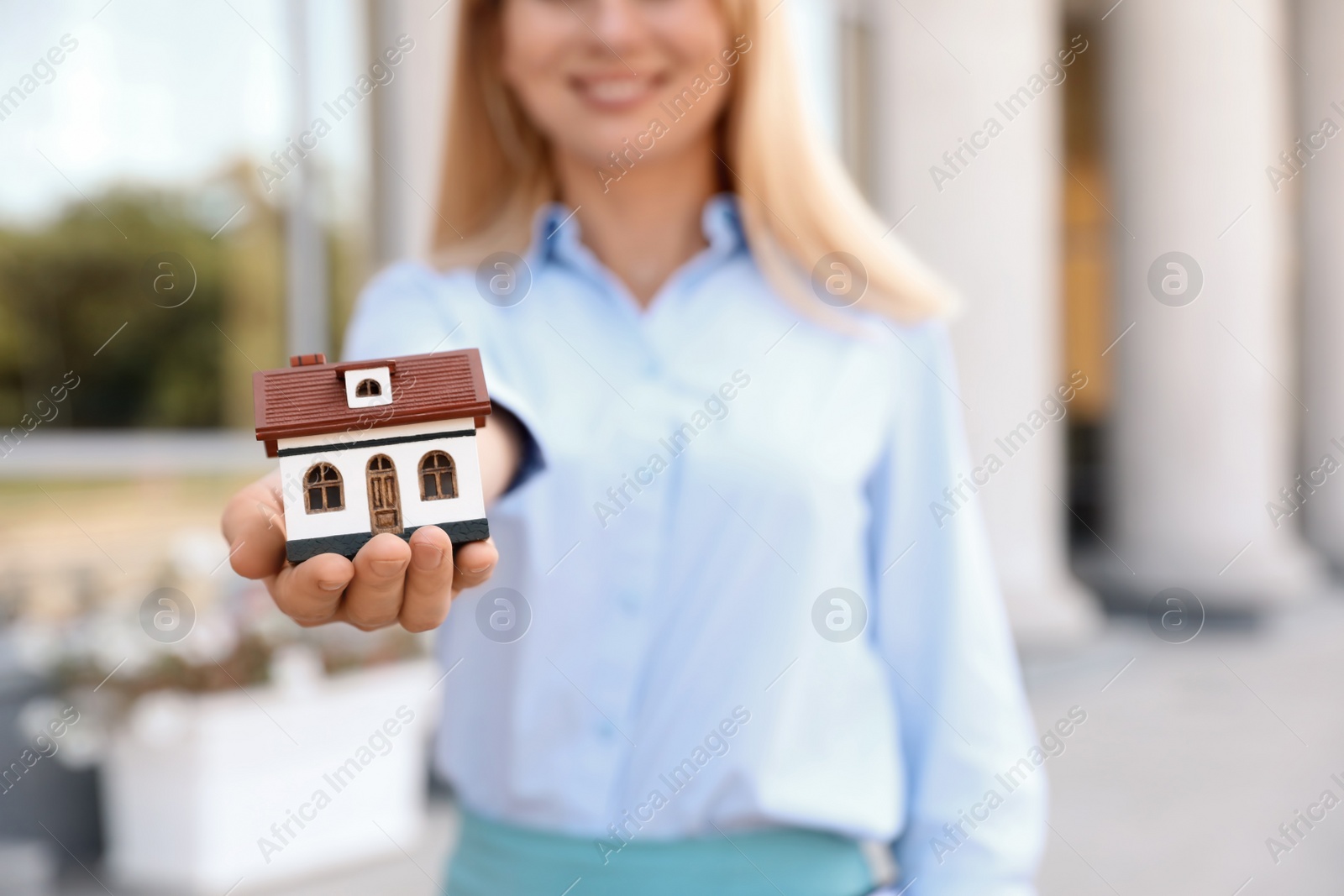 Photo of Female real estate agent with house model outdoors